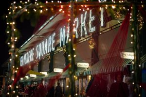 Belvedere Square sign at night during Christmas, surrounded by lights and ribbons.